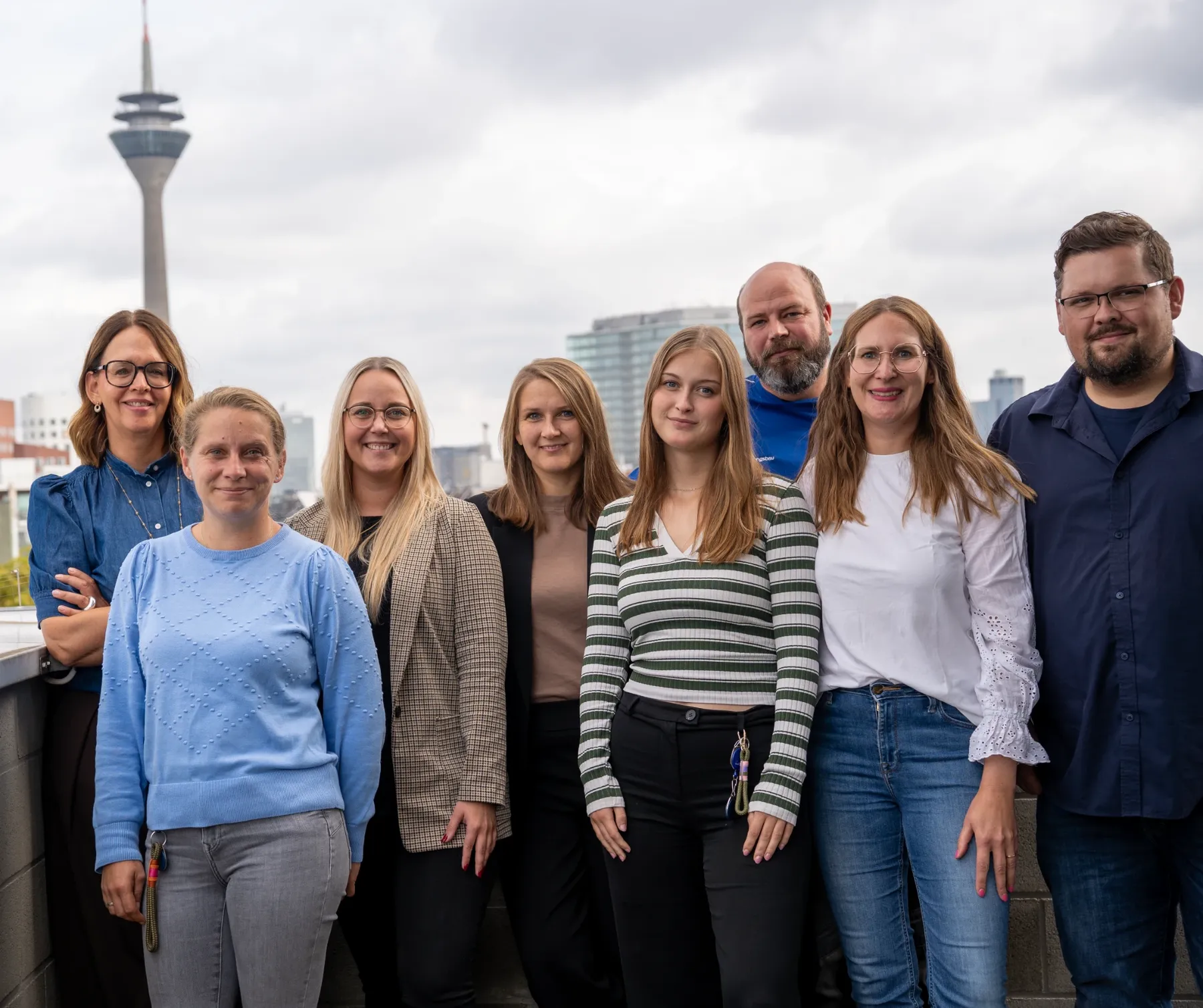 Das Customer Experience Team der Rheinwohnungsbau vor der Düsseldorfer Skyline mit dem Rheinturm